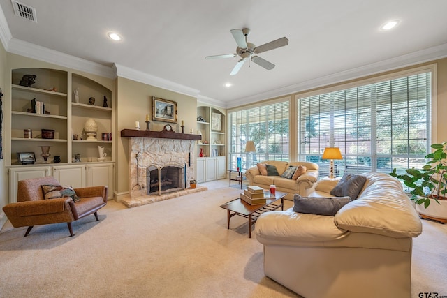 living room with a stone fireplace, light colored carpet, ceiling fan, crown molding, and built in features