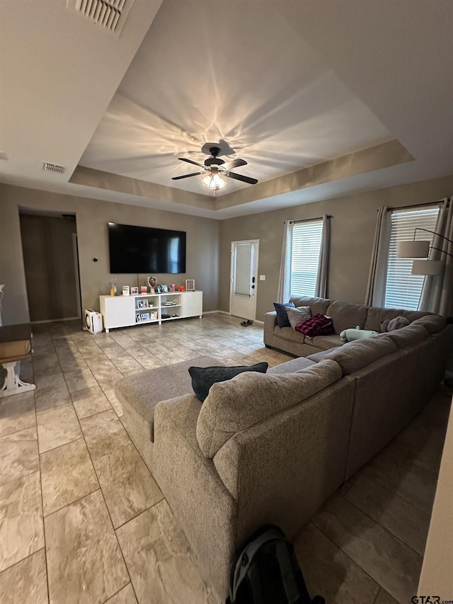 living area with visible vents, a ceiling fan, and a tray ceiling