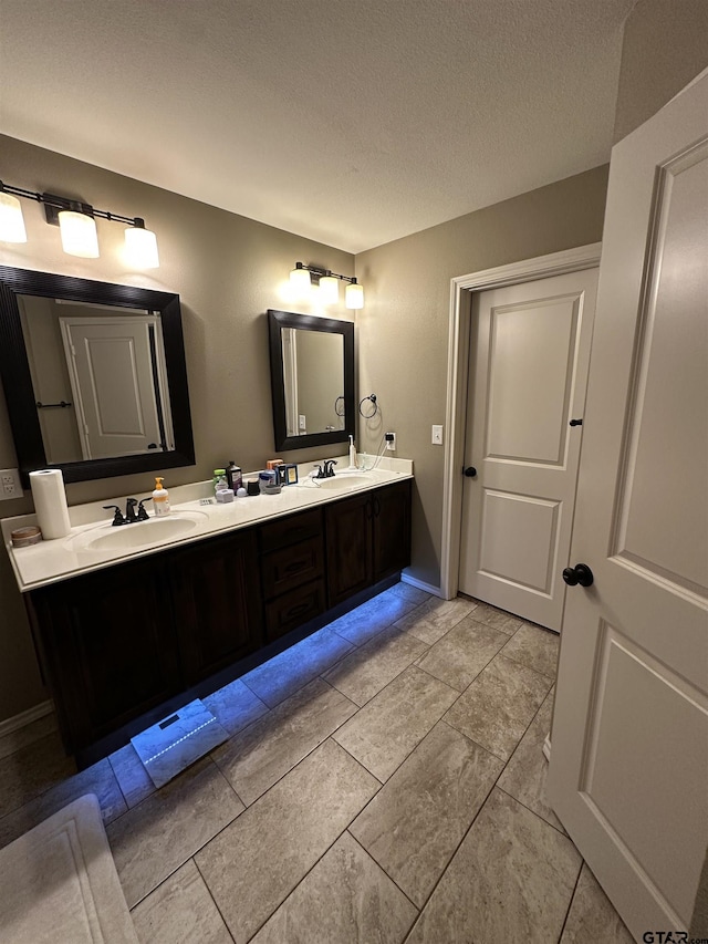full bath with a textured ceiling, double vanity, and a sink