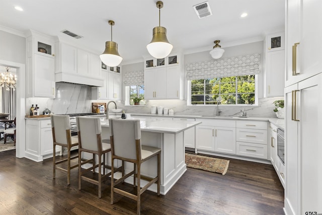 kitchen featuring a center island with sink, white cabinetry, hanging light fixtures, and dark wood-type flooring