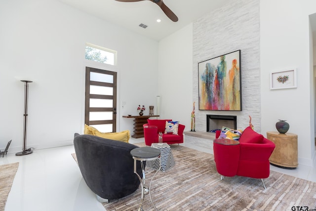 living room featuring ceiling fan, a towering ceiling, and a fireplace