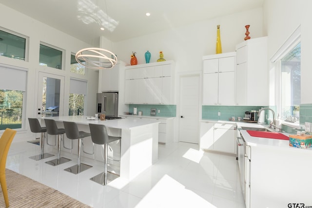 kitchen featuring white cabinetry, backsplash, hanging light fixtures, high quality fridge, and a kitchen island