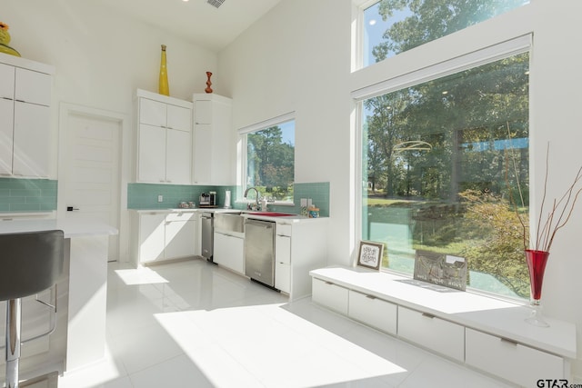 kitchen with white cabinetry, decorative backsplash, a high ceiling, stainless steel dishwasher, and light tile patterned floors