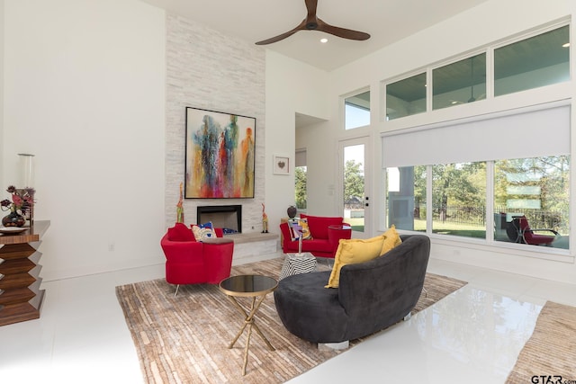 living room with ceiling fan, a towering ceiling, and a stone fireplace