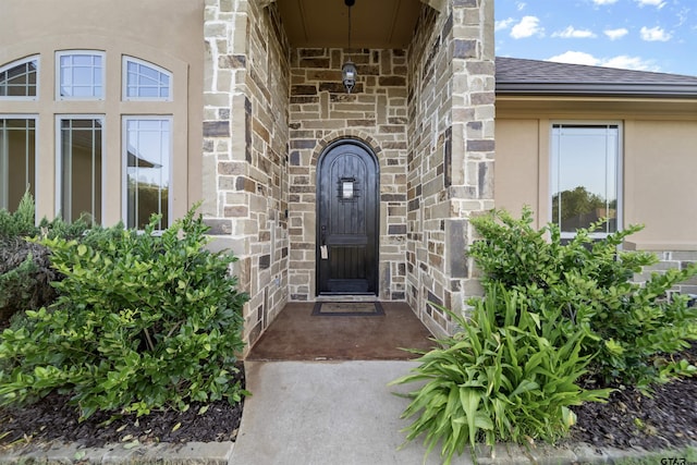 entrance to property featuring stone siding, a shingled roof, brick siding, and stucco siding