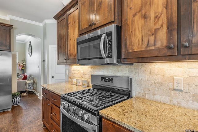 kitchen with appliances with stainless steel finishes, tasteful backsplash, light stone counters, ornamental molding, and dark hardwood / wood-style floors