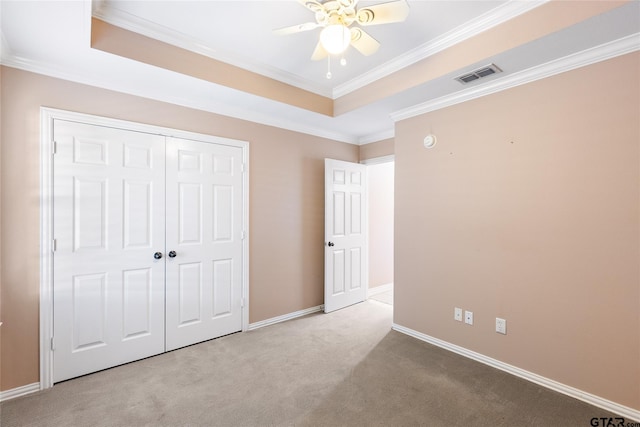 unfurnished bedroom featuring light carpet, ceiling fan, a tray ceiling, a closet, and ornamental molding