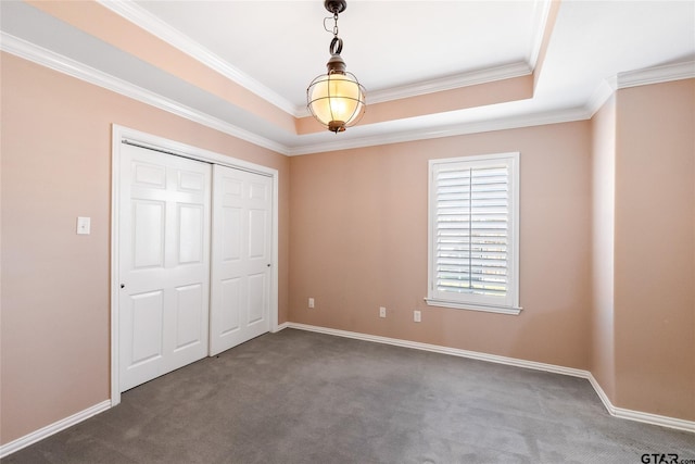 unfurnished bedroom with a raised ceiling, a closet, crown molding, and dark carpet