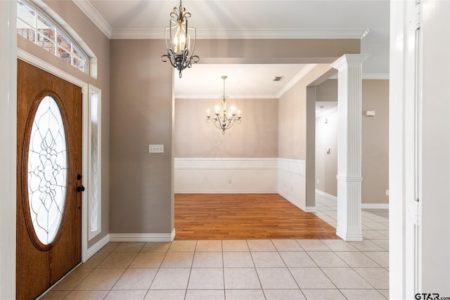 tiled entryway with a notable chandelier, crown molding, and decorative columns