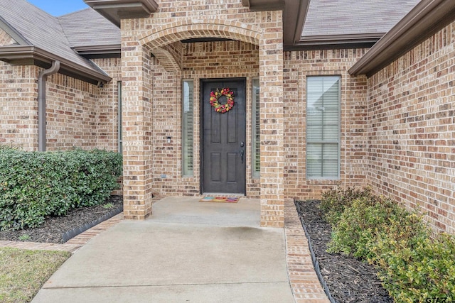 entrance to property featuring a shingled roof and brick siding