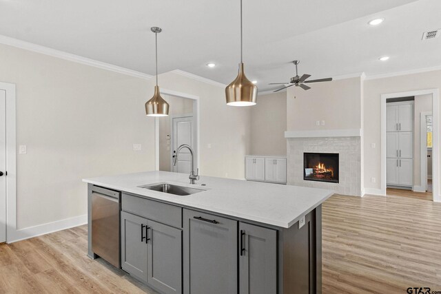 kitchen with light wood-type flooring, hanging light fixtures, sink, and an island with sink