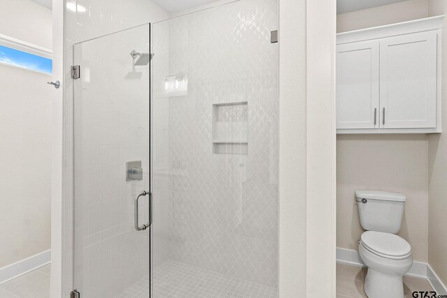 bathroom featuring a shower with shower door, tile patterned floors, and toilet