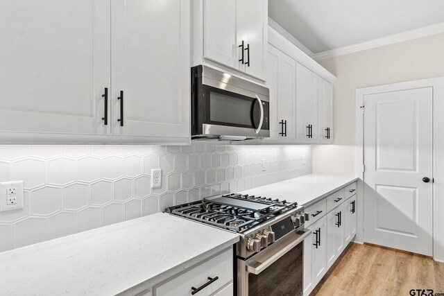 kitchen with light hardwood / wood-style floors, appliances with stainless steel finishes, crown molding, white cabinets, and decorative backsplash