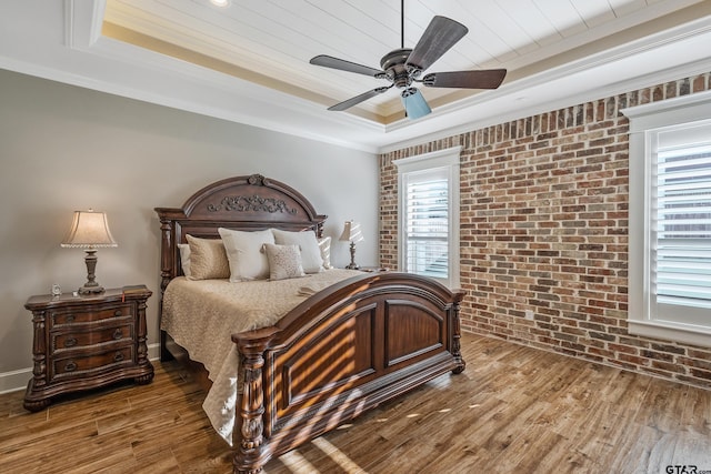 bedroom featuring hardwood / wood-style floors, ornamental molding, ceiling fan, a raised ceiling, and brick wall