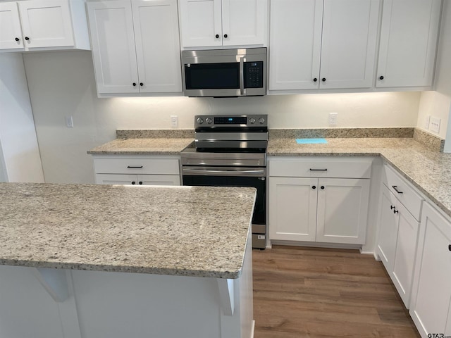 kitchen with hardwood / wood-style flooring, stainless steel appliances, white cabinetry, and light stone countertops