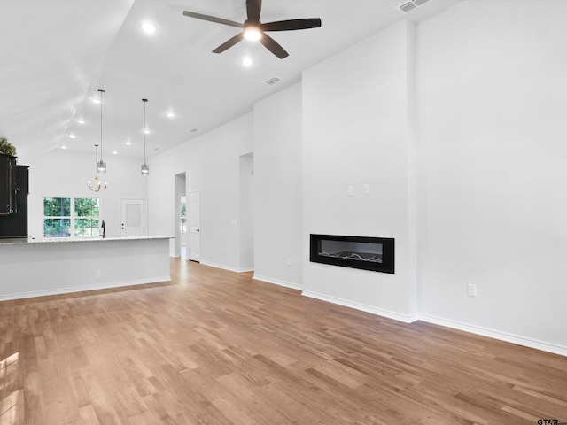 unfurnished living room featuring ceiling fan with notable chandelier, high vaulted ceiling, and light hardwood / wood-style floors