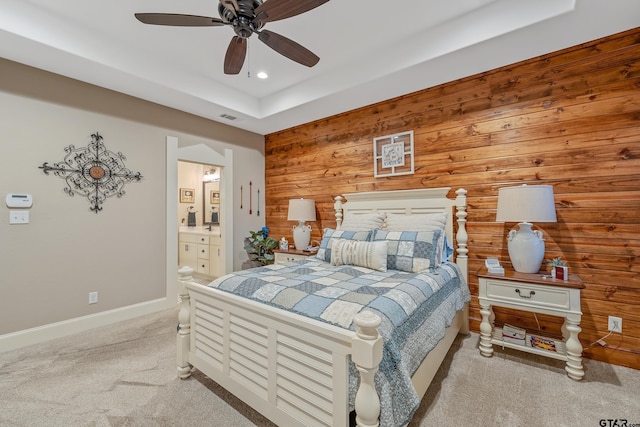 bedroom with light carpet, connected bathroom, ceiling fan, and wooden walls