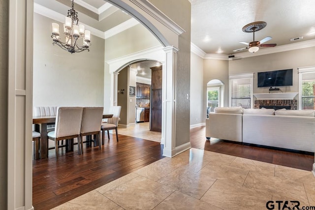 living room with crown molding, ceiling fan with notable chandelier, arched walkways, a fireplace, and baseboards