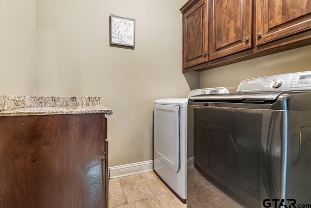 clothes washing area with baseboards, washer and dryer, and cabinet space