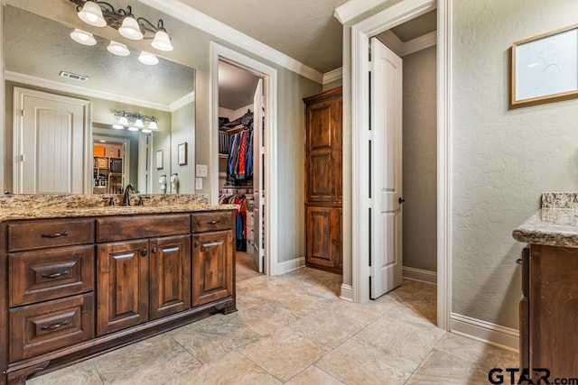 bathroom featuring baseboards, visible vents, ornamental molding, vanity, and a walk in closet