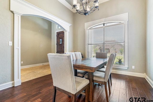dining space featuring arched walkways, an inviting chandelier, baseboards, dark wood-type flooring, and ornate columns
