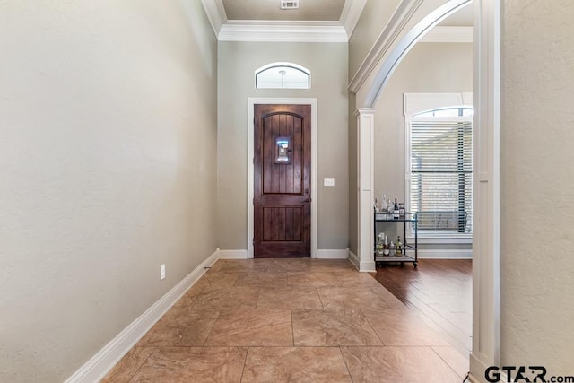 foyer featuring arched walkways, baseboards, a healthy amount of sunlight, and crown molding