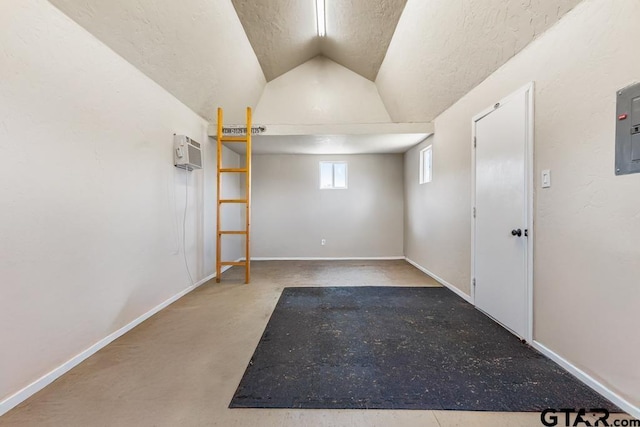 empty room with vaulted ceiling, baseboards, a textured ceiling, and a wall mounted air conditioner