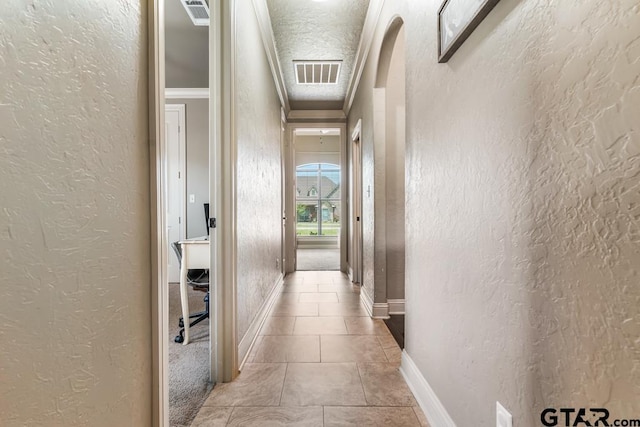 corridor with a textured wall, crown molding, and visible vents