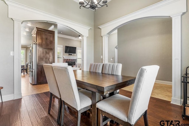dining space featuring arched walkways, a brick fireplace, and decorative columns