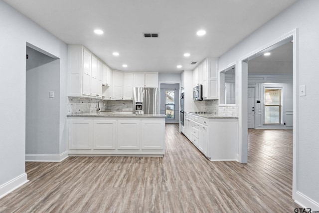 kitchen with plenty of natural light, white cabinets, stainless steel appliances, and light hardwood / wood-style floors