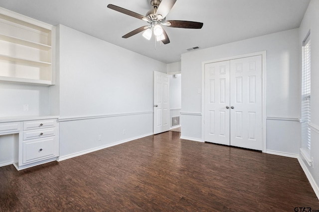 unfurnished bedroom featuring ceiling fan, built in desk, dark wood-type flooring, and a closet