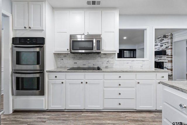 kitchen featuring decorative backsplash, light stone countertops, light wood-type flooring, appliances with stainless steel finishes, and white cabinetry