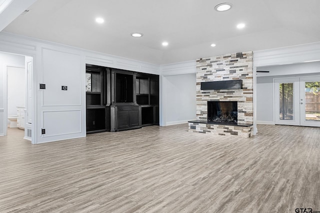 unfurnished living room featuring a stone fireplace, crown molding, french doors, and light wood-type flooring