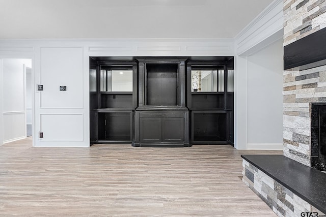 interior space featuring a stone fireplace, light hardwood / wood-style floors, and ornamental molding