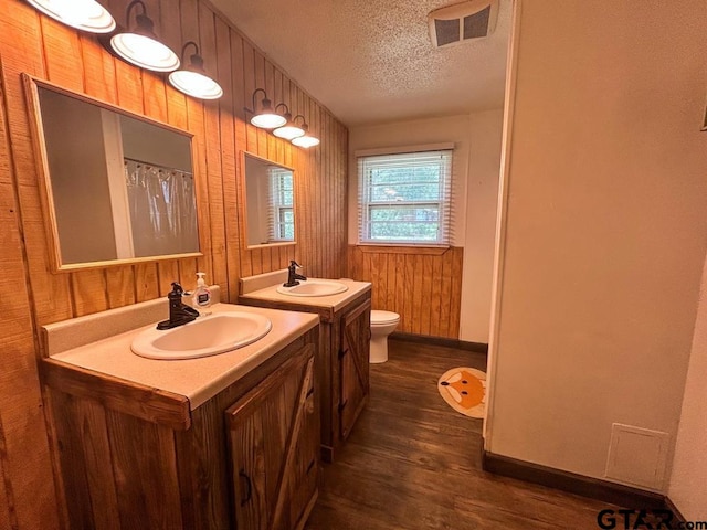 bathroom with toilet, hardwood / wood-style floors, wood walls, a textured ceiling, and vanity