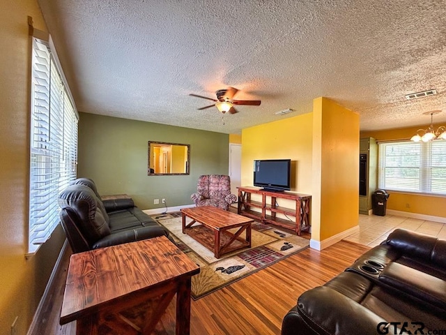 living room featuring light hardwood / wood-style floors, ceiling fan with notable chandelier, and a textured ceiling