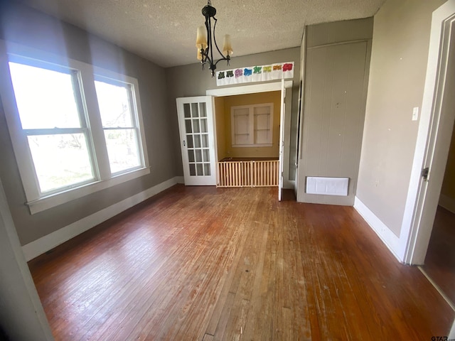 unfurnished dining area featuring hardwood / wood-style flooring, a textured ceiling, and a notable chandelier