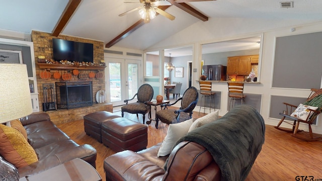 living room with french doors, vaulted ceiling with beams, a stone fireplace, light hardwood / wood-style floors, and ceiling fan