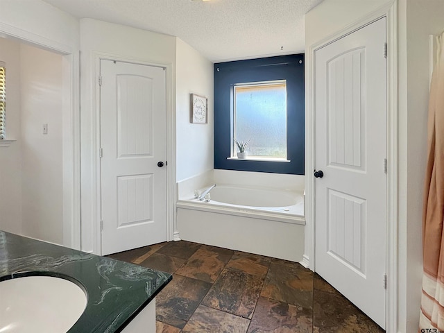 bathroom featuring stone tile floors, a garden tub, and a textured ceiling