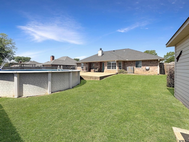 rear view of house with fence, a yard, central AC, brick siding, and roof with shingles