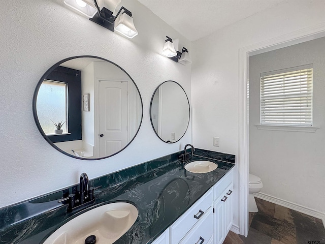 bathroom with stone finish floor, a sink, double vanity, and toilet