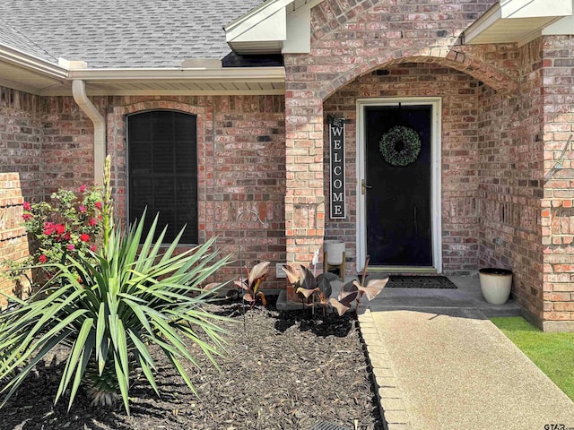 doorway to property featuring brick siding and a shingled roof