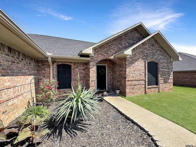 view of front of home with brick siding, a shingled roof, and a front yard