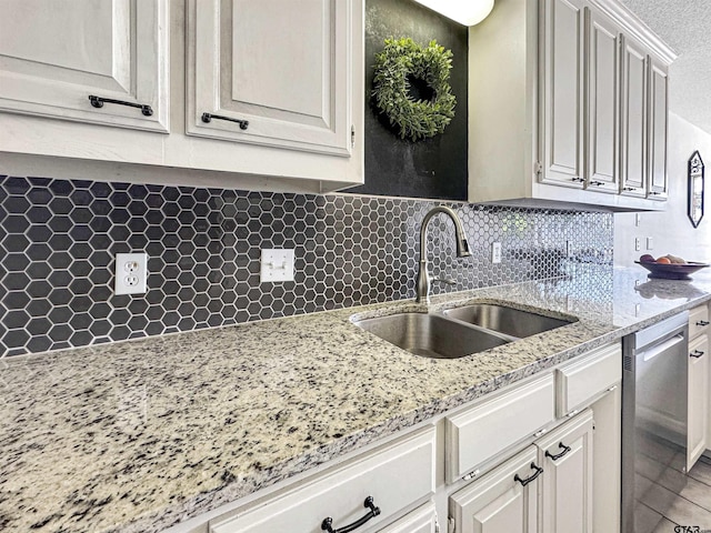 kitchen with dishwasher, decorative backsplash, light stone countertops, and a sink