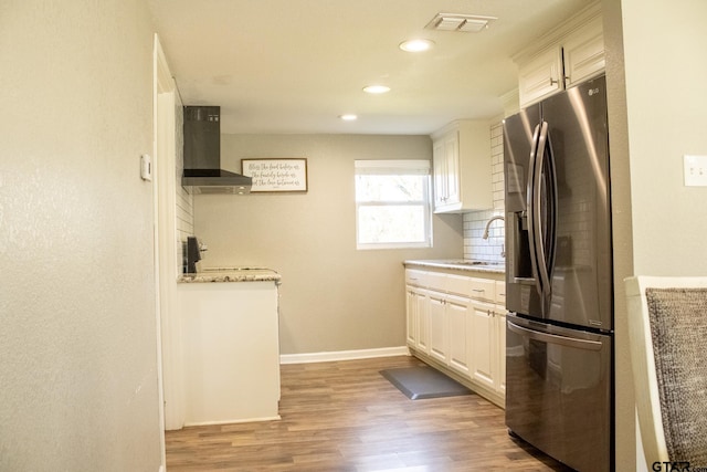 kitchen with visible vents, a sink, stainless steel refrigerator with ice dispenser, wall chimney exhaust hood, and backsplash