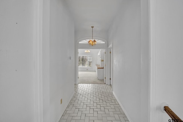 corridor featuring an inviting chandelier, baseboards, and brick floor