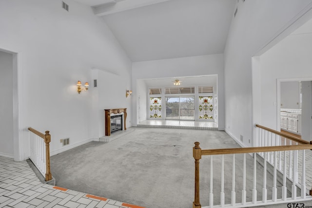 unfurnished living room with carpet floors, a glass covered fireplace, high vaulted ceiling, beamed ceiling, and baseboards