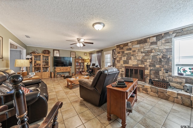 living room with visible vents, a textured ceiling, a stone fireplace, light tile patterned floors, and ceiling fan