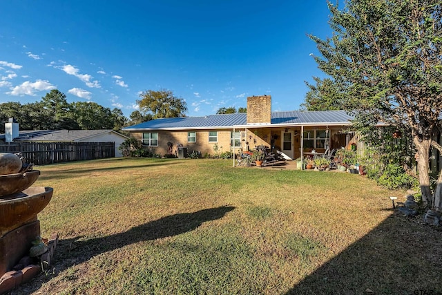 back of property with fence, a lawn, a chimney, metal roof, and a patio area