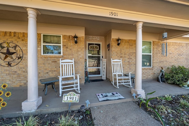 view of exterior entry featuring brick siding and covered porch